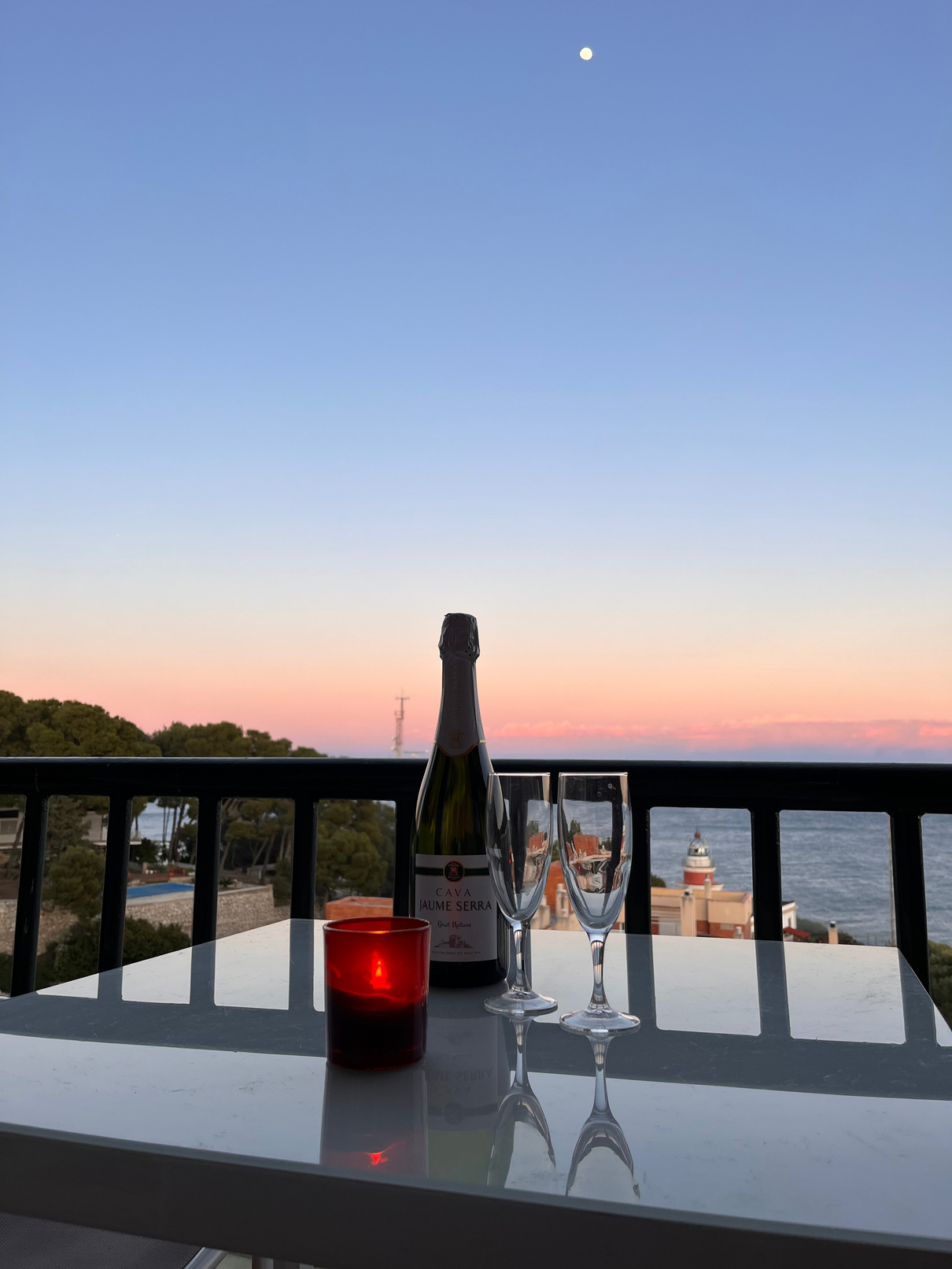 Copa de cava en la terraza al atardecer con el faro al fondo